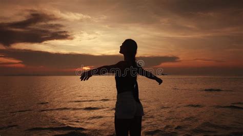 Silhouette Of Young Female At Orange Sunset Raising Hands In Air