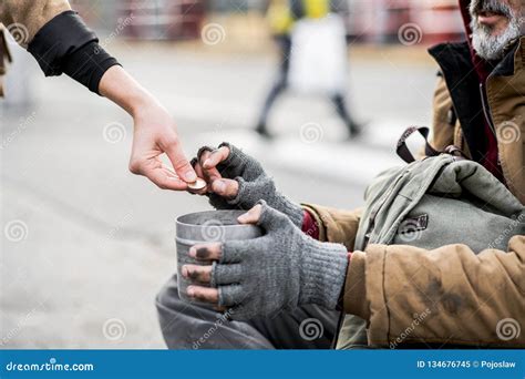 A Midsection Of Woman Giving Money To Homeless Beggar Man Sitting In