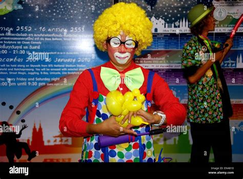 Bangkok, Thailand: Clown in a curly yellow wig making balloon animals on a BTS Skytrain walkway ...