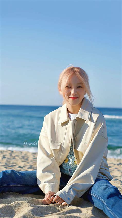 A Woman Sitting On Top Of A Sandy Beach Next To The Ocean With Her