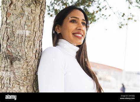 Positive Indian Female With Black Hair Leaning On Tree With Blurred