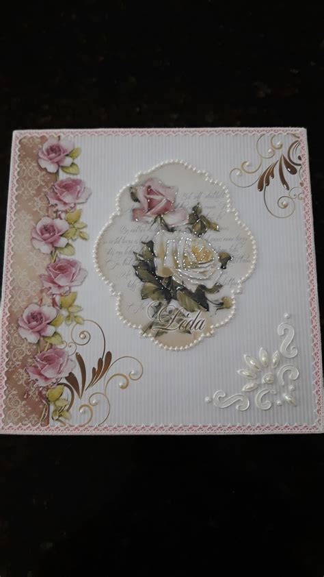 A White Card With Pink Roses And Gold Trimmings On It Sitting On A Table