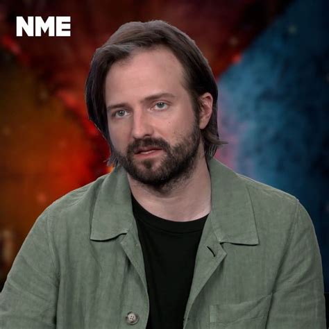 a man with long hair and beard sitting in front of an orange background ...