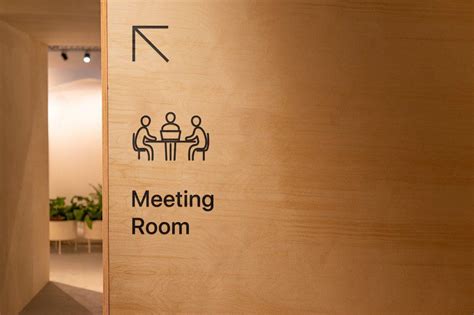 The meeting room black sign on the wooden wall with direction sign and text. Office signage for ...