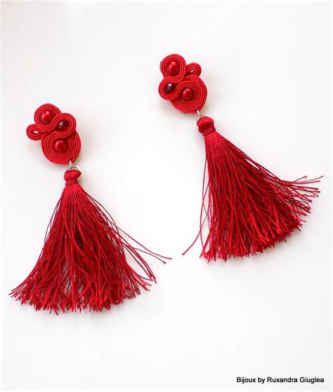 Two Pairs Of Red Tasseled Earrings On A White Surface