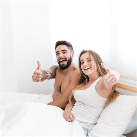 Jeune Couple Assis Sur Le Lit Gesticulant Pouce En Lair Photo Gratuite