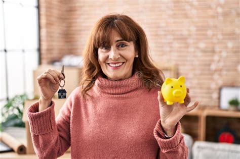 Middle Age Hispanic Woman Holding Piggy Bank And House Keys Smiling