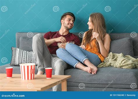 Young Couple Eating Popcorn While Watching Tv On Sofa At Home Stock