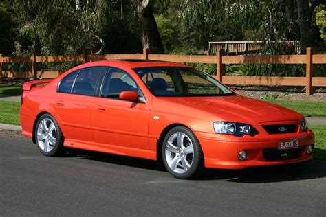 An Orange Car Is Parked On The Side Of The Road In Front Of A Fence