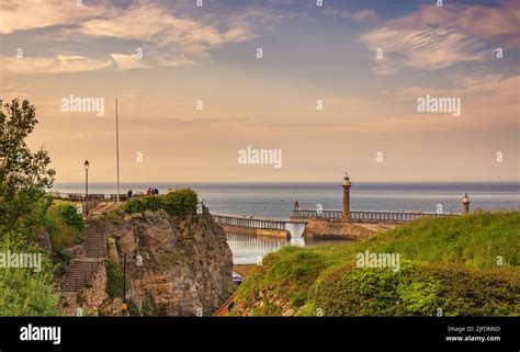 A Pier And A Lighthouse Seen Through A Gap Between Two Cliffs An