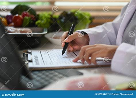 Side View Of Nutritionist Writing Diet Plan And Using Laptop At Desk