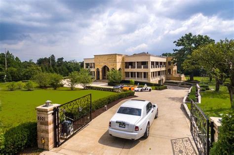 A White Car Is Parked In Front Of A Large House With A Driveway And Gate