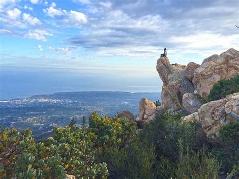 a person sitting on top of a large rock near some trees and bushes with ...