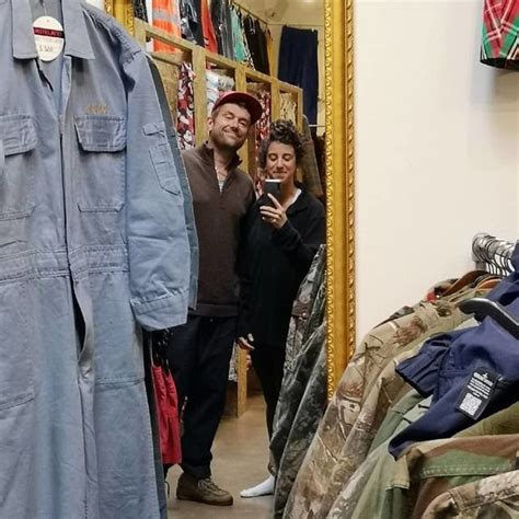 Two People Standing In Front Of A Mirror Looking At Their Cell Phones