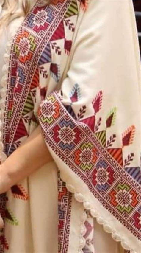 A Woman Wearing A White Dress With Colorful Designs On It S Sleeves And