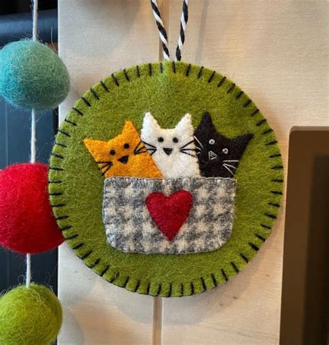 A Green Felt Decoration With Three Cats In A Basket And Two Balls Hanging From The Ceiling