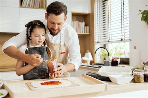 Curious Daughter With Young Father Pouring Tomato Sauce On Prepared