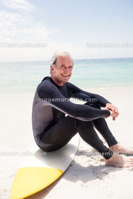 Portrait of happy senior man in wetsuit sitting on surfboardの写真素材