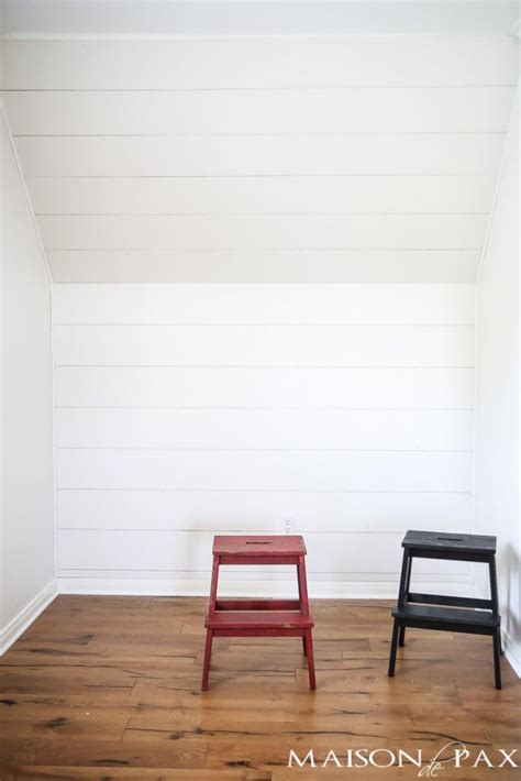 Two Small Stools Sit In The Corner Of A Room With White Walls And Wood Flooring