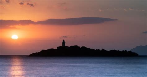 Silhueta de um farol no mar contra o céu durante o pôr do sol Foto