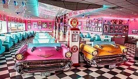 Two Vintage Cars Are Parked In A Diner With Checkered Flooring And Neon