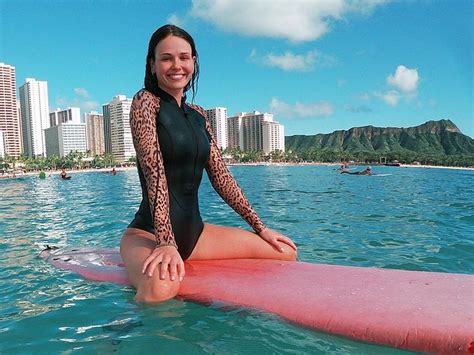 a woman is sitting on a surfboard in the water with buildings behind her and blue sky