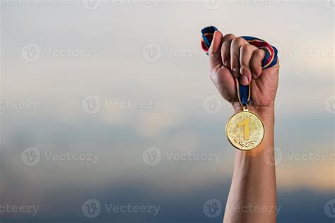 mão segurando a medalha de ouro contra o fundo do céu nublado do