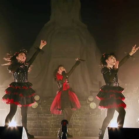 Three Girls In Black And Red Outfits On Stage With Their Hands Up To