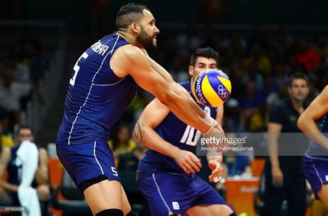 Two Men In Blue Uniforms Playing Volleyball On A Court With People