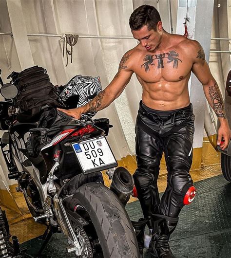 A Shirtless Man Standing Next To A Motorcycle With Tattoos On His Arm