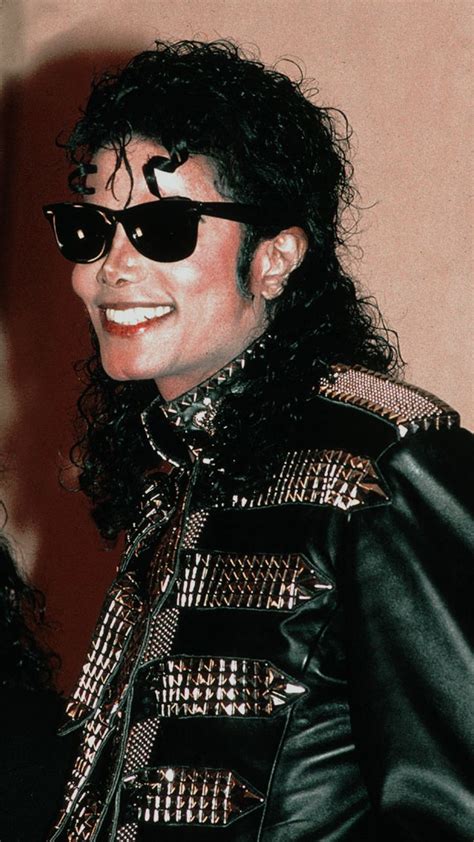 Michael Jackson Dressed In Black And Gold With Sunglasses On His Head Smiling At The Camera