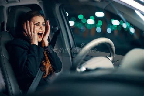 Frightened Woman Is Sitting Behind The Wheel Of A Car In A Black Shirt Wearing A Seat Belt