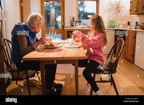 Side View Of A Grandmother And Her Granddaughter Sitting At The Dining