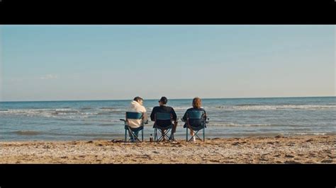 Three People Sitting On Chairs At The Beach Looking Out Over The Water