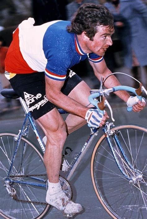 A Man Riding On The Back Of A Bike Down A Street Next To A Crowd