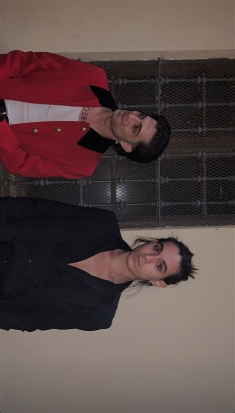 Two Men Standing Next To Each Other In Front Of A Wall With Metal Grates