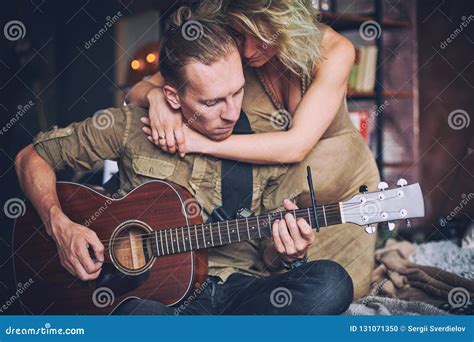 Man Playing A Guitar And His Pregnant Wife Are Sitting On A Bed In A