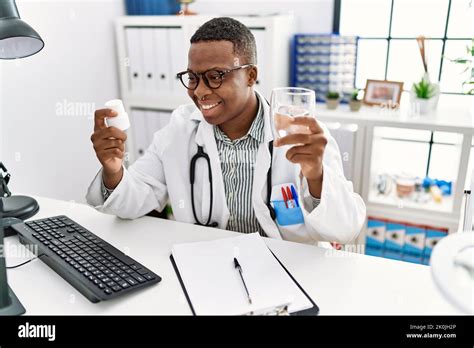 Young African Man Working As Doctor Holding Pills And Water At Medical