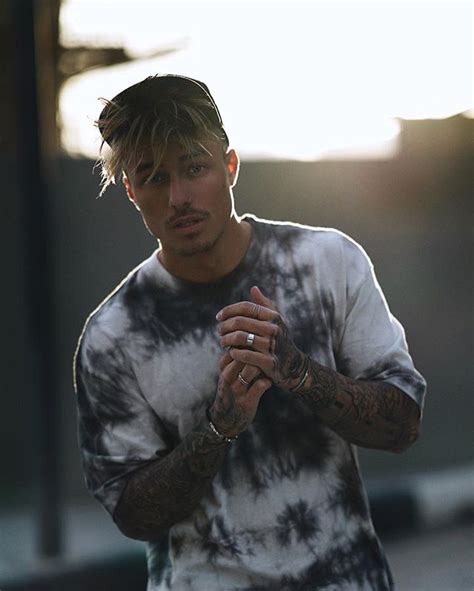 A Man With Tattoos Standing In Front Of A Street Sign And Holding His