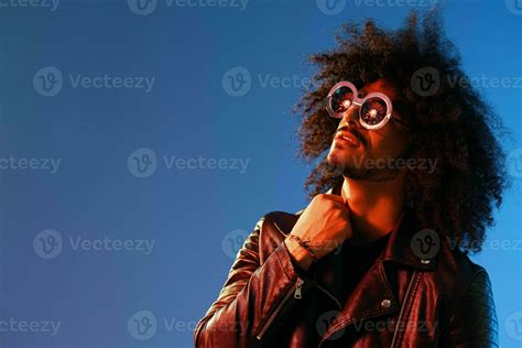 Portrait of a stylish man with curly hair with glasses smile on blue ...