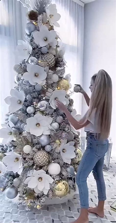 A Woman Decorating A Christmas Tree With Silver And White Ornaments