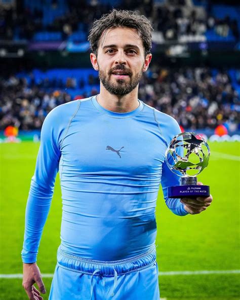 A Man Holding A Soccer Ball And Trophy In Front Of A Large Stadium