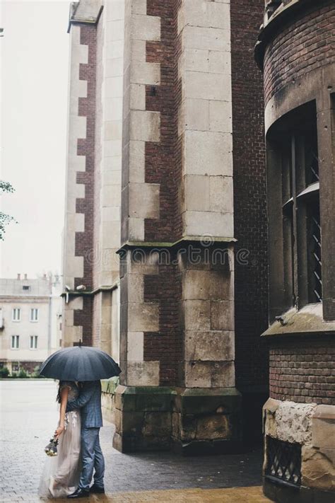 Stylish Bride And Groom Walking Under Umbrella And Kissing On