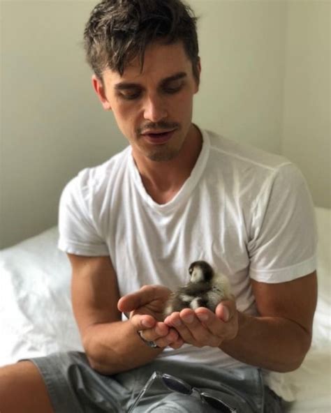 A Man Sitting On A Bed Holding A Small Bird In His Hands And Looking At The Camera