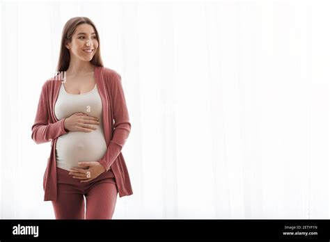 Beautiful Smiling Pregnant Woman Standing Near Window At Home Touching