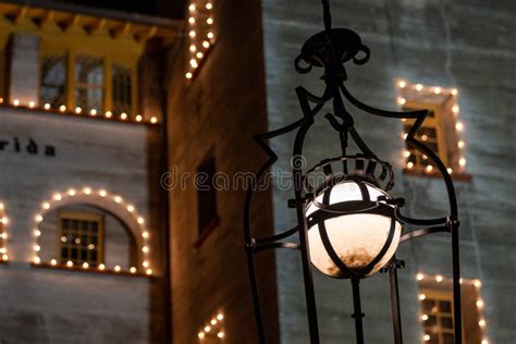 Lamp Post Illuminated At Night Against A Building Decorated With