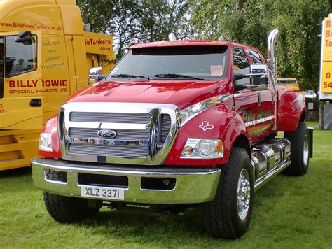 A Large Red Truck Parked On Top Of A Lush Green Field Next To Yellow Trucks