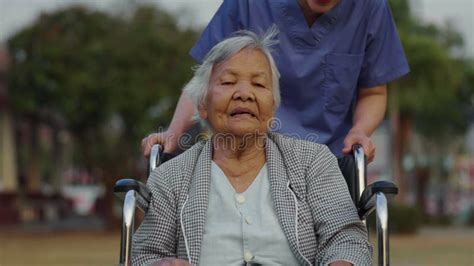 Nurse Take Care And Pushing Senior Woman In Wheelchair At Park