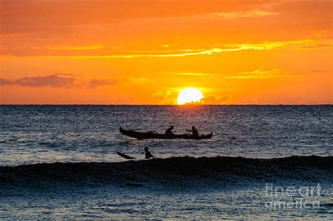 Two Men Paddling A Hawaiian Outrigger Canoe At Sunset On Maui