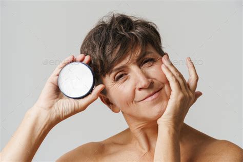 Mature Half Naked Woman Smiling While Applying Face Cream Stock Photo